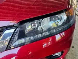 Close-up image of a like-new, shiny car headlight on a vehicle in Davie, Florida. The headlight lens is clear and polished, reflecting sunlight and the surrounding environment. The sleek, well-maintained appearance suggests recent cleaning or headlight restoration.