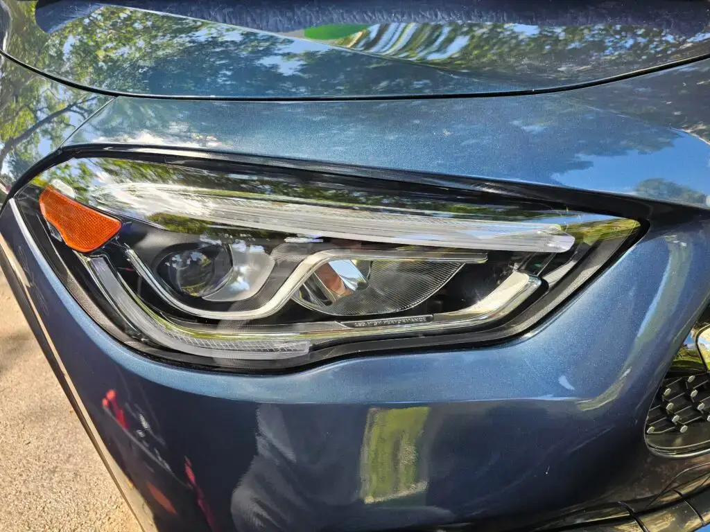 Close-up image of a like-new, shiny car headlight on a vehicle in Pembroke Park, Florida. The headlight lens is clear and polished, reflecting sunlight and the surrounding environment. The sleek, well-maintained appearance suggests recent cleaning or headlight restoration.