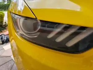 Close-up image of a like-new, shiny car headlight on a vehicle in Doral, Florida. The headlight lens is clear and polished, reflecting sunlight and the surrounding environment. The sleek, well-maintained appearance suggests recent cleaning or headlight restoration.