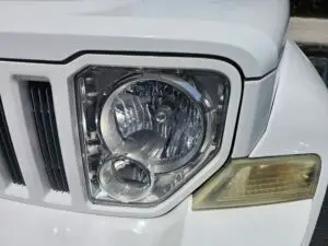 Close-up image of a like-new, shiny car headlight on a vehicle in Lauderdale Lakes, Florida. The headlight lens is clear and polished, reflecting sunlight and the surrounding environment. The sleek, well-maintained appearance suggests recent cleaning or headlight restoration.