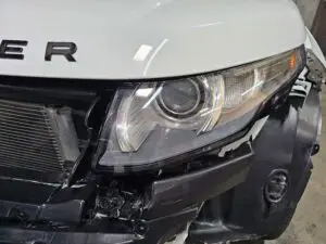 Close-up image of a like-new, shiny car headlight on a vehicle in Lauderhill, Florida. The headlight lens is clear and polished, reflecting sunlight and the surrounding environment. The sleek, well-maintained appearance suggests recent cleaning or headlight restoration.