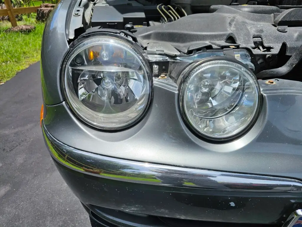 Close-up image of a like-new, shiny car headlight on a vehicle in Miami Springs, Florida. The headlight lens is clear and polished, reflecting sunlight and the surrounding environment. The sleek, well-maintained appearance suggests recent cleaning or headlight restoration.