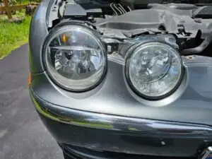 Close-up image of a like-new, shiny car headlight on a vehicle in Miami Springs, Florida. The headlight lens is clear and polished, reflecting sunlight and the surrounding environment. The sleek, well-maintained appearance suggests recent cleaning or headlight restoration.