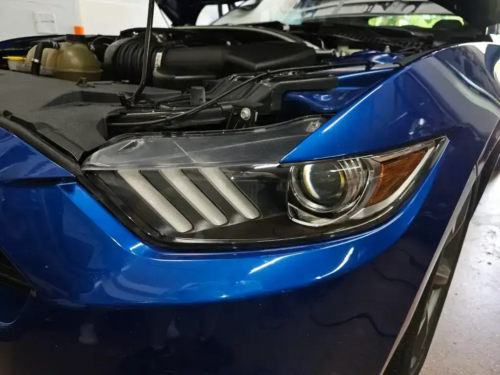 Close-up image of a like-new, shiny car headlight on a vehicle in North Lauderdale, Florida. The headlight lens is clear and polished, reflecting sunlight and the surrounding environment. The sleek, well-maintained appearance suggests recent cleaning or headlight restoration.