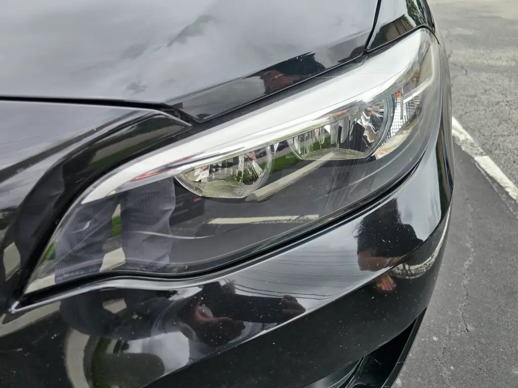 Close-up image of a like-new, shiny car headlight on a vehicle in Parkland, Florida. The headlight lens is clear and polished, reflecting sunlight and the surrounding environment. The sleek, well-maintained appearance suggests recent cleaning or headlight restoration.