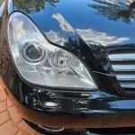 Close-up image of a like-new, shiny car headlight on a vehicle in Cooper City, Florida. The headlight lens is clear and polished, reflecting sunlight and the surrounding environment. The sleek, well-maintained appearance suggests recent cleaning or headlight restoration.