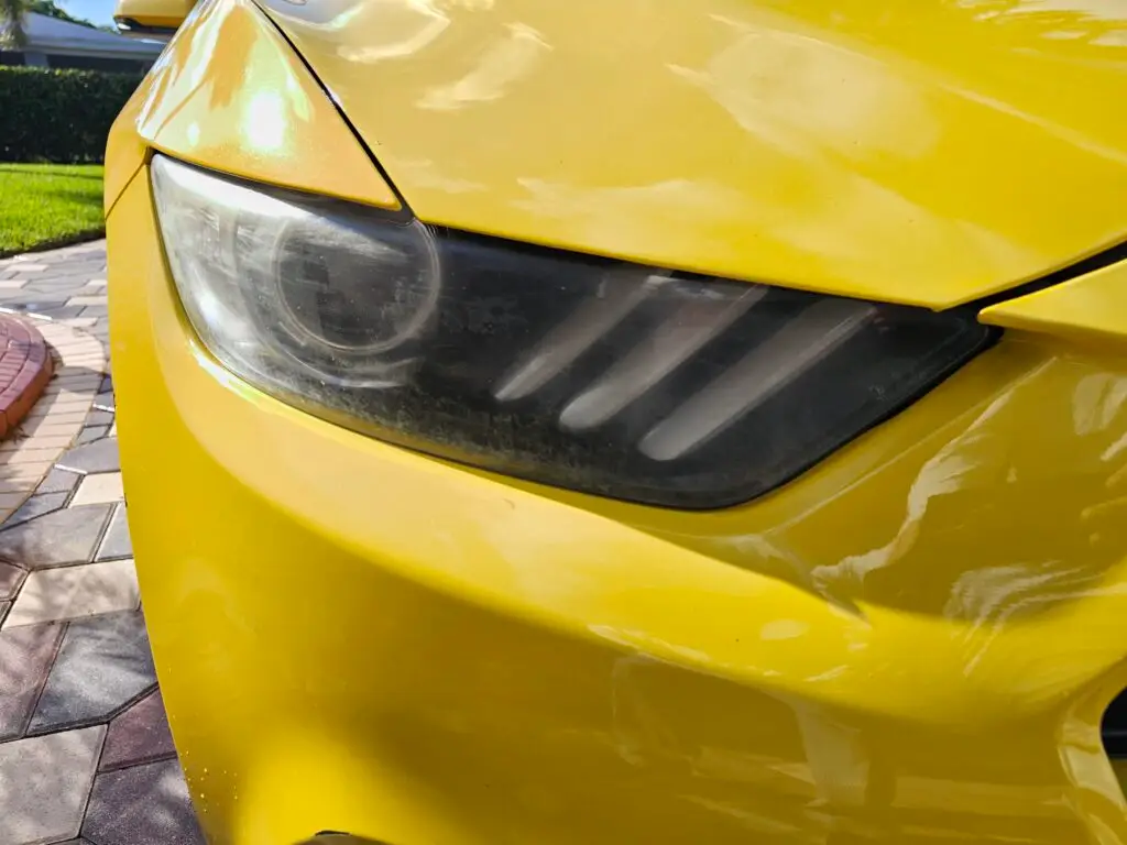 Close-up image of a faded and cloudy car headlight on a vehicle in Doral, Florida. The headlight lens appears dull and foggy, likely due to oxidation or wear over time, and needs a headlight restoration