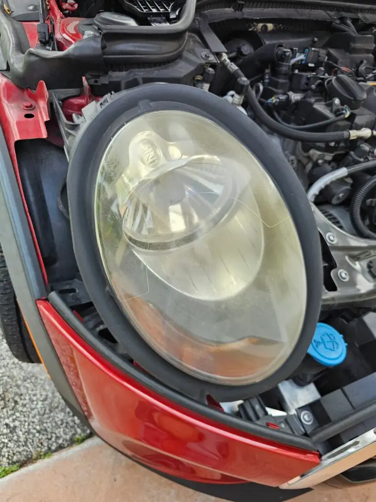 Close-up image of a faded and cloudy car headlight on a vehicle in Hollywood, Florida. The headlight lens appears dull and foggy, likely due to oxidation or wear over time, and needs a headlight restoration.