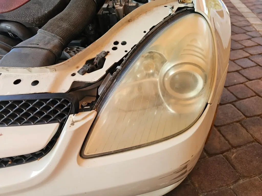 Close-up image of a faded and cloudy car headlight on a vehicle in Margate, Florida. The headlight lens appears dull and foggy, likely due to oxidation or wear over time, and needs a headlight restoration.