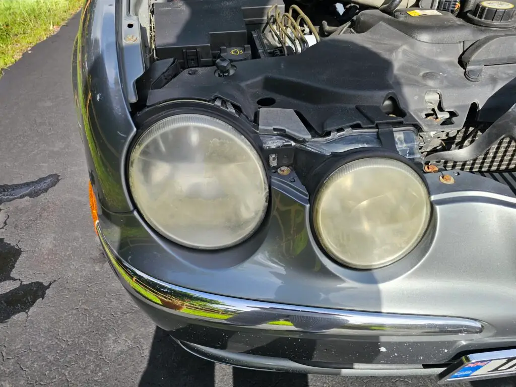 Close-up image of a faded and cloudy car headlight on a vehicle in Miami Springs, Florida. The headlight lens appears dull and foggy, likely due to oxidation or wear over time, and needs a headlight restoration.