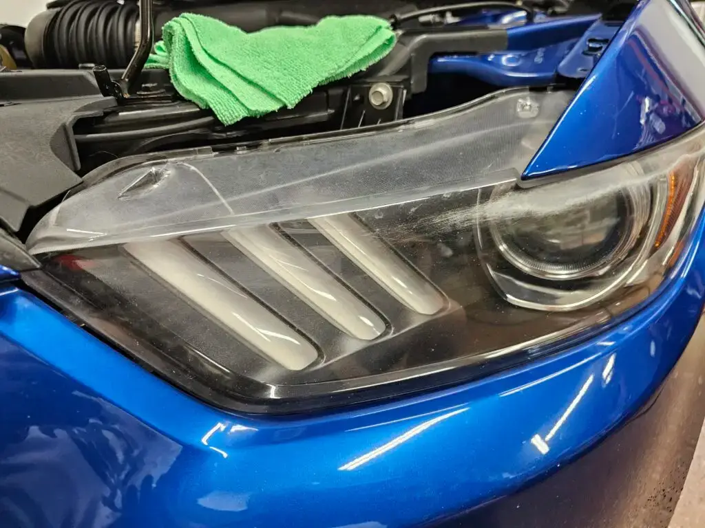 Close-up image of a faded and cloudy car headlight on a vehicle in North Lauderdale, Florida. The headlight lens appears dull and foggy, likely due to oxidation or wear over time, and needs a headlight restoration.
