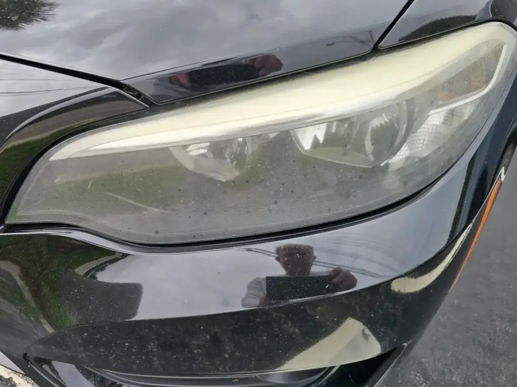 Close-up image of a faded and cloudy car headlight on a vehicle in Parkland, Florida. The headlight lens appears dull and foggy, likely due to oxidation or wear over time, and needs a headlight restoration.