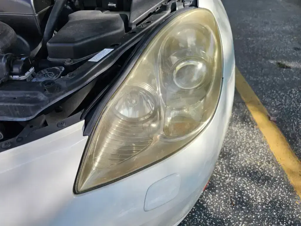 Close-up image of a faded and cloudy car headlight on a vehicle in Plantation, Florida. The headlight lens appears dull and foggy, likely due to oxidation or wear over time, and needs a headlight restoration.