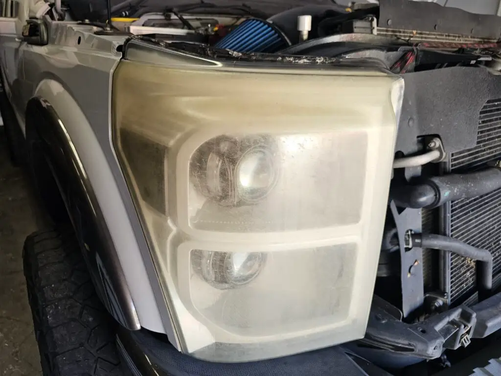 Close-up image of a faded and cloudy car headlight on a vehicle in Sunrise, Florida. The headlight lens appears dull and foggy, likely due to oxidation or wear over time, and needs a headlight restoration.