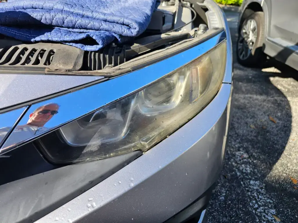 Close-up image of a faded and cloudy car headlight on a vehicle in Weston, Florida. The headlight lens appears dull and foggy, likely due to oxidation or wear over time, and needs a headlight restoration.