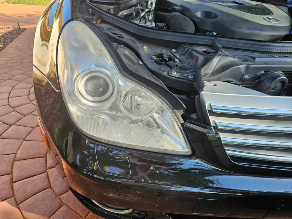 Close-up image of a faded and cloudy car headlight on a vehicle in Cooper City, Florida. The headlight lens appears dull and foggy, likely due to oxidation or wear over time, and needs a headlight restoration