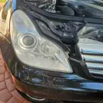 Close-up image of a faded and cloudy car headlight on a vehicle in Cooper City, Florida. The headlight lens appears dull and foggy, likely due to oxidation or wear over time, and needs a headlight restoration