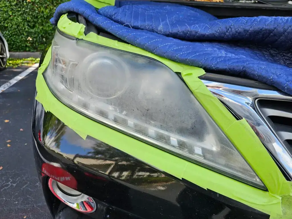 Close-up image of a faded and cloudy car headlight on a vehicle in Fort Lauderdale, Florida. The headlight lens appears dull and foggy, likely due to oxidation or wear over time, and needs a headlight restoration.